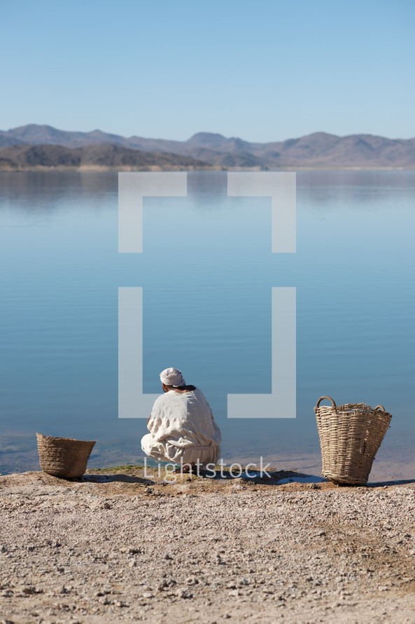 man standing beside baskets by a sea