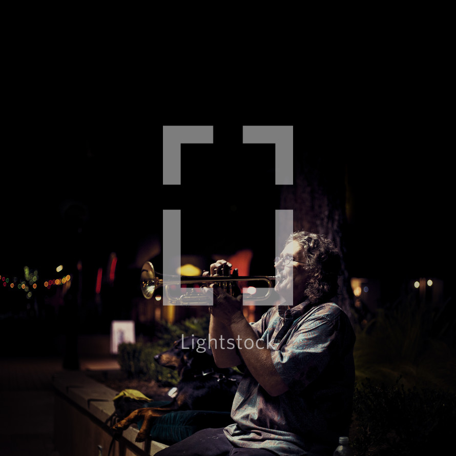 A man playing a trumpet on the street at night 