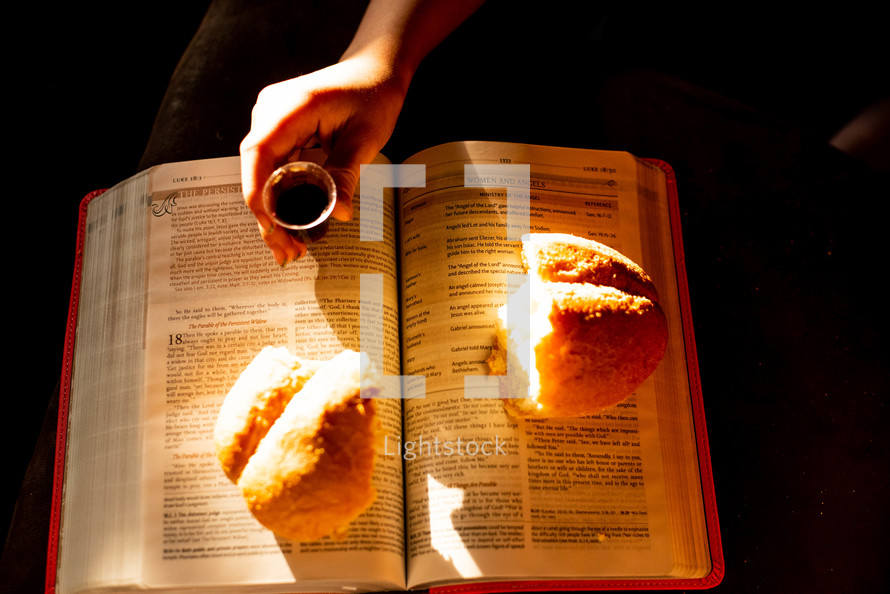 A child holding a communion cup over a Bible with broken bread.