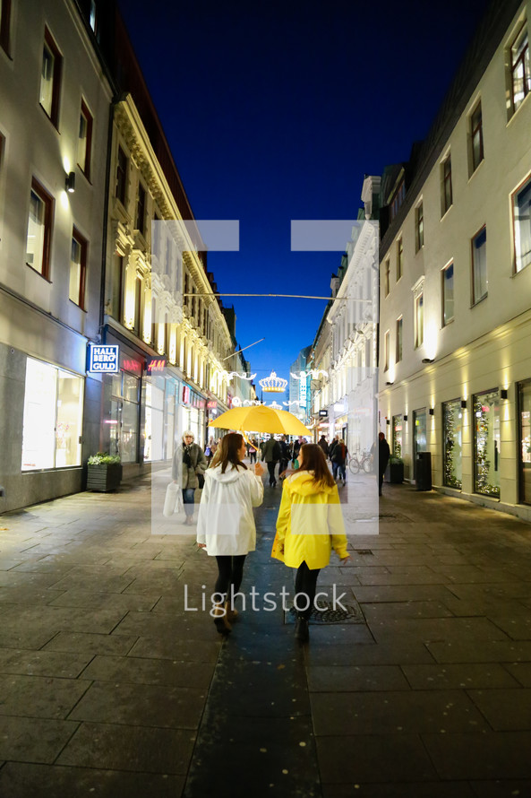 women with rain jackets and an umbrella walking down an alley at night in a city 