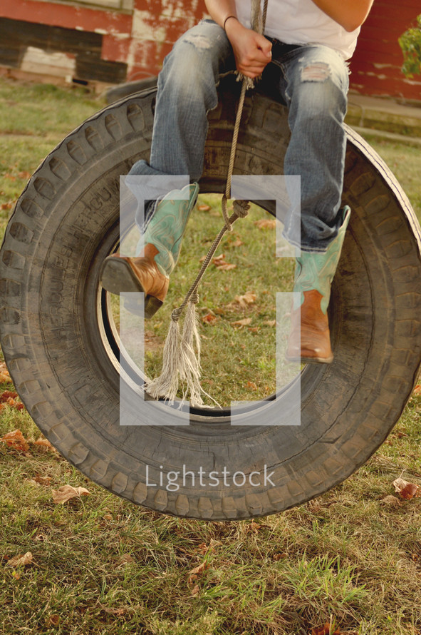 A person sitting on a tire swing with cowboy boots