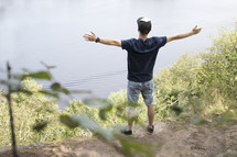 Teenager standing high on cliff overlooking lake with arms outstretched