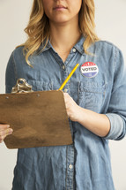 A young woman with a clipboard and pencil wearing an "I Voted" button.