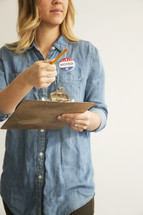 A young woman with a clipboard and pencil and an "I Voted" button.