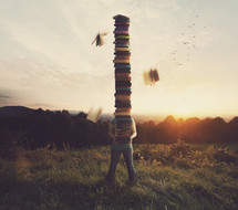 Person in a field balancing a very tall stack of books.