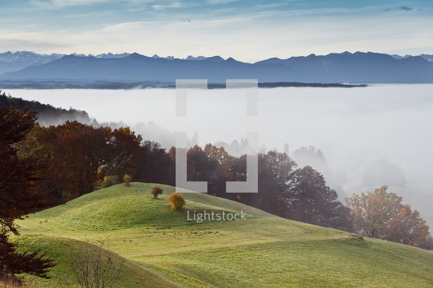 Alps mountain range and green grass on rolling hills 
