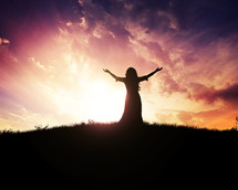 Silhouette of woman with arms raised on a hilltop under a purple and orange sky.