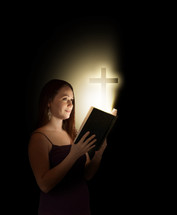 woman holding a glowing Bible with a cross