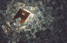 A Bible with glowing pages sits among piles of money.