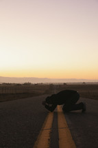 a man kneeling in the middle of a road praying 
