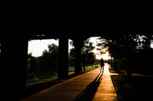 a silhouette of a woman standing on a trail under an overpass 
