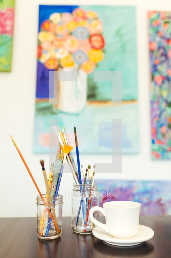 Paintbrushes in jars and paintings on the wall.