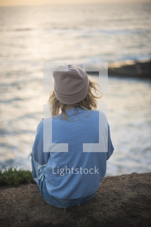 a woman sitting on a shore looking out at the water 