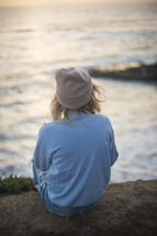a woman sitting on a shore looking out at the water 