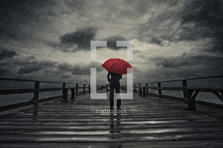 man standing on a pier in the rain with a red umbrella