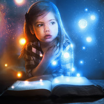 A little girl watches glowing lights and stars flow out of an open book