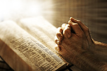 Prayers hands on open Bible.