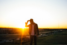 man touching his hat standing outdoors at sunset 