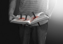 A man holding an open Bible with spikes through it and bloodstained.