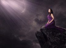 light shining on a woman on a rock in a purple dress 