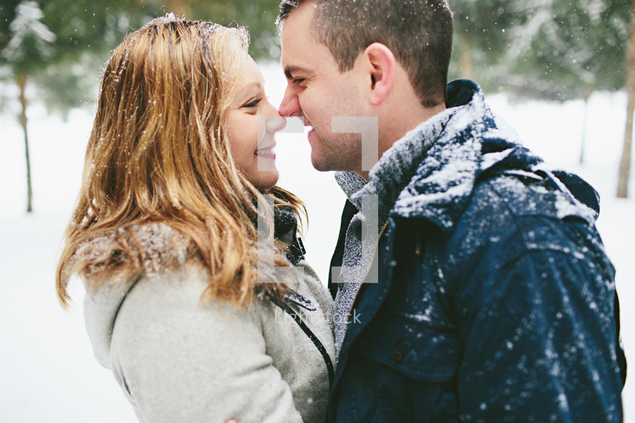 a couple nose to nose standing outdoors in snow 