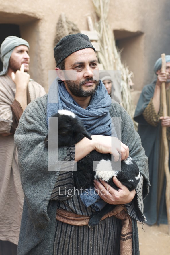 man holding a goat in a village set in Biblical times 