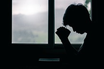silhouette of a young man praying with head bowed 