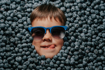 Smiling boy in sunglesses surrounded by blueberries
