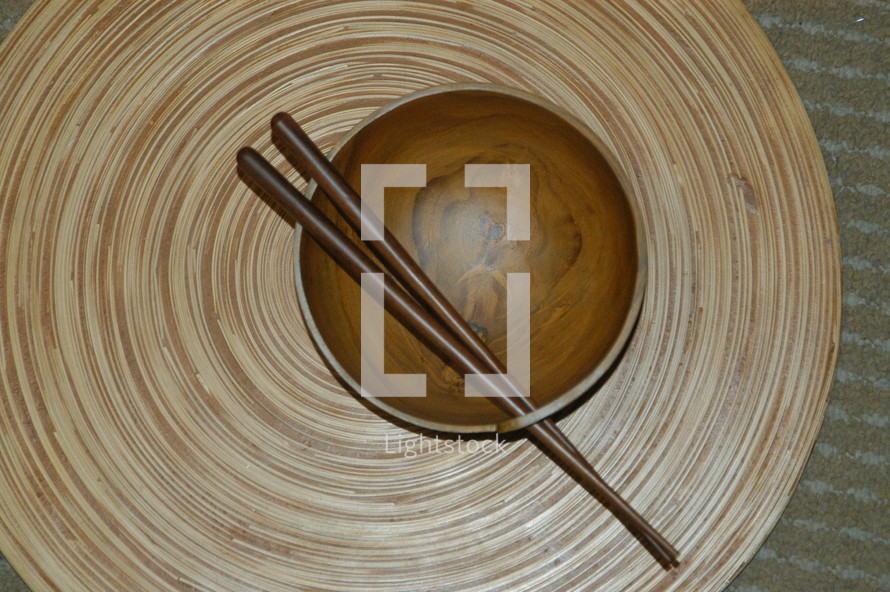 chop sticks resting on a wooden bowl on a bamboo mat