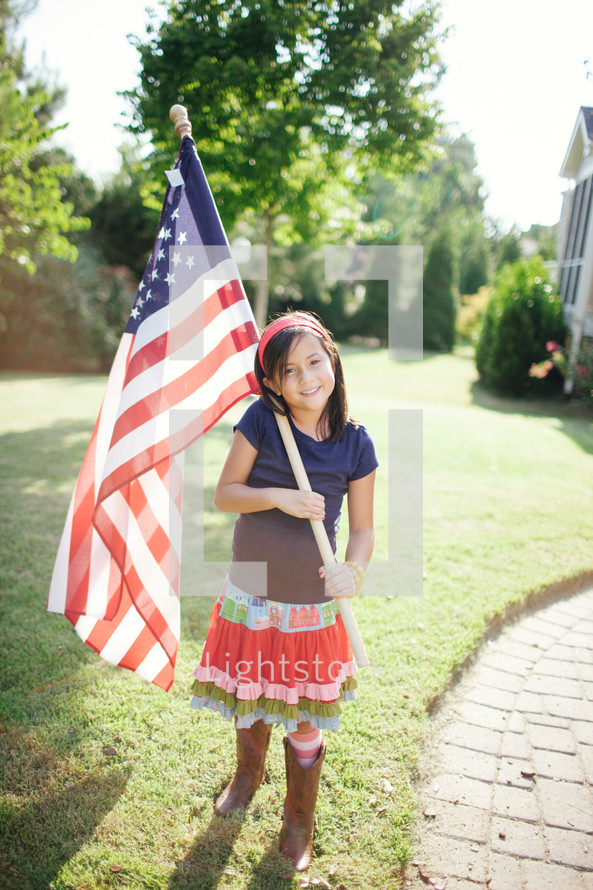 girl child holding an American flag in front of her house