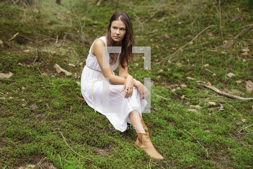 a young woman in a dress sitting on mossy ground 