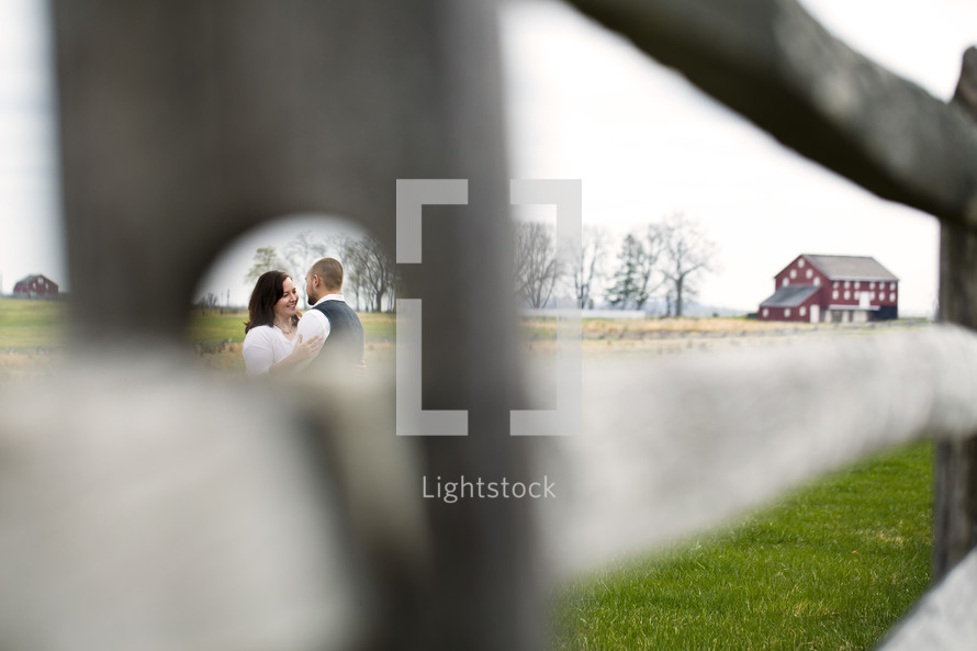 couple hugging outdoors through a hole in a fence post 