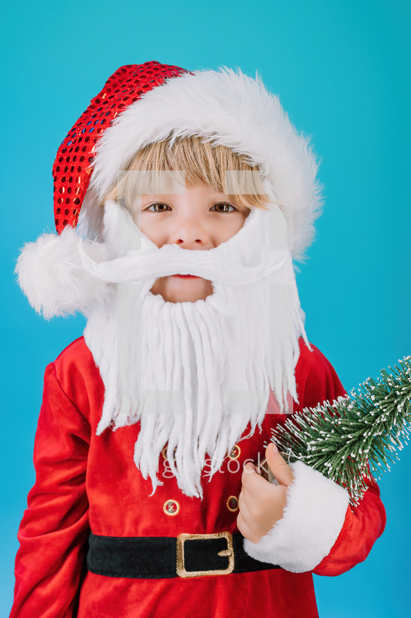 Friendly little Christmas boy in Santa Claus costume on blue background. Happy emotional child with artificial beard. High quality photo