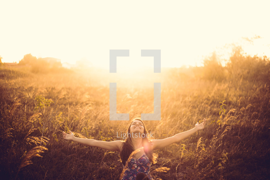 A woman with open arms standing in a field full of glowing sunlight. 