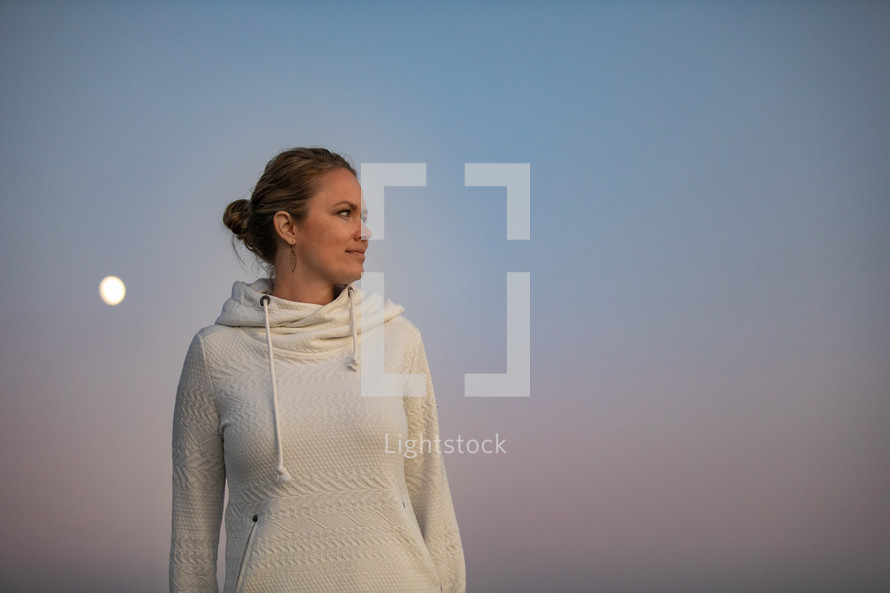 woman in a sweatshirt standing outdoors at dusk 
