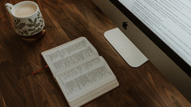 open Bible on a desk and computer screen on a desk 