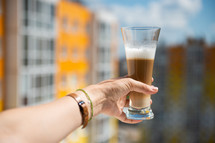 multilayer coffee or cappuccino in a glass of coffee on a woman's hand stretched out into the window against the background of an apartment building