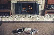 headphones, tablet, open Bible, pen, journal, and coffee cup by a fireplace 