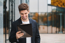 Portrait of young handsome man in jacket with documents, utility bills, report. Businessman near office building. He is satisfied with work of corporate staff. High quality photo