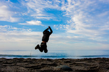 man in a coat jumping on a beach 