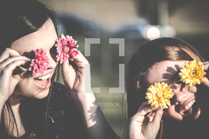 Two girls covering their eyes with flowers.