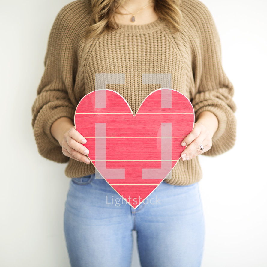 a woman holding a red wooden Valentine's Day heart 
