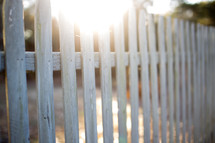 Sun shining on a white picket fence.