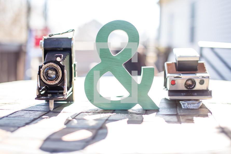 Two old cameras and a ampersand sign, all sitting on a table