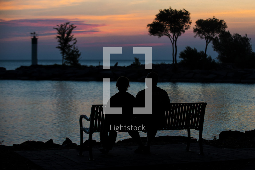 silhouette of a man and woman looking out at lake water at sunset