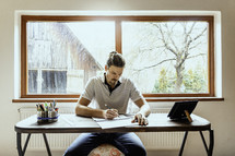 a man sitting at a desk drawing with a farm scene behind him 