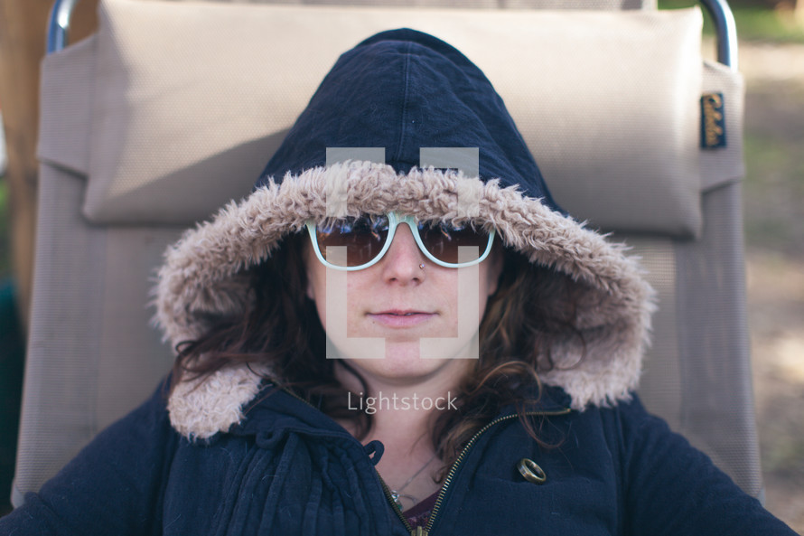 a woman in a hooded coat lying in a lounge chair 
