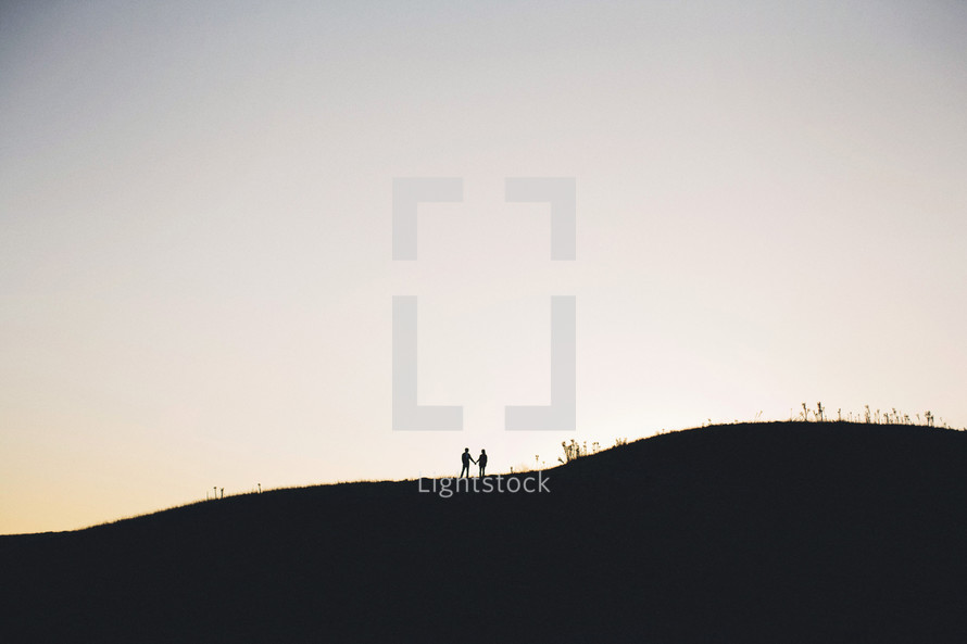 silhouette of a distant couple standing on a hill holding hands
