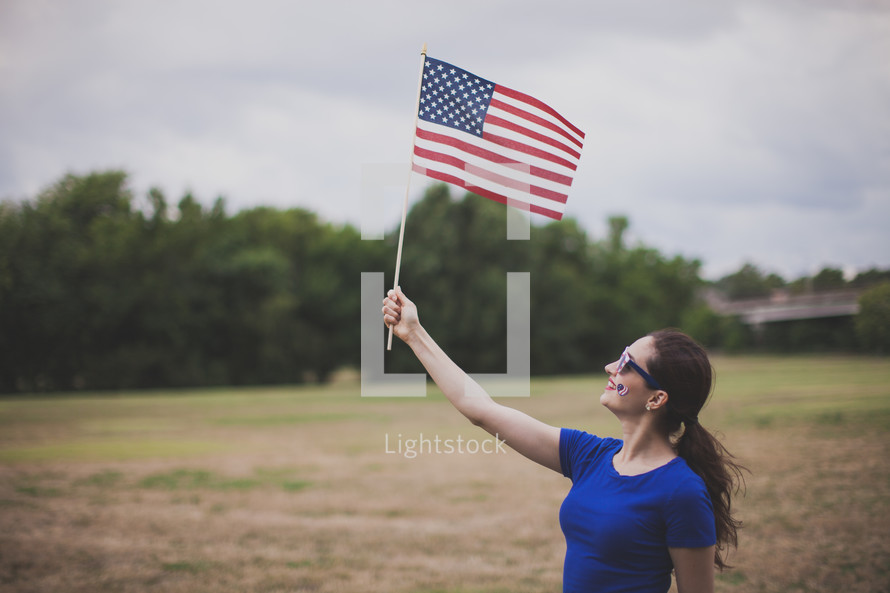 woman wearing stars and stripes sunglasses and a temporary tattoo - holding an American flag