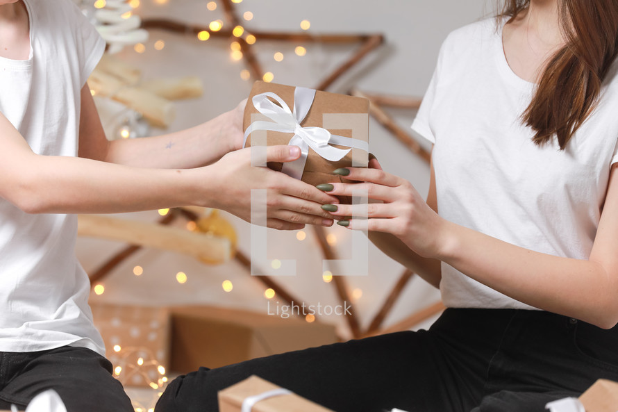 Cropped photo of man had giving a gift box to woman on lights garlands background. christmas and new year concept. young boyfriend is giving surprise in box with white ribbon to his girlfriend.